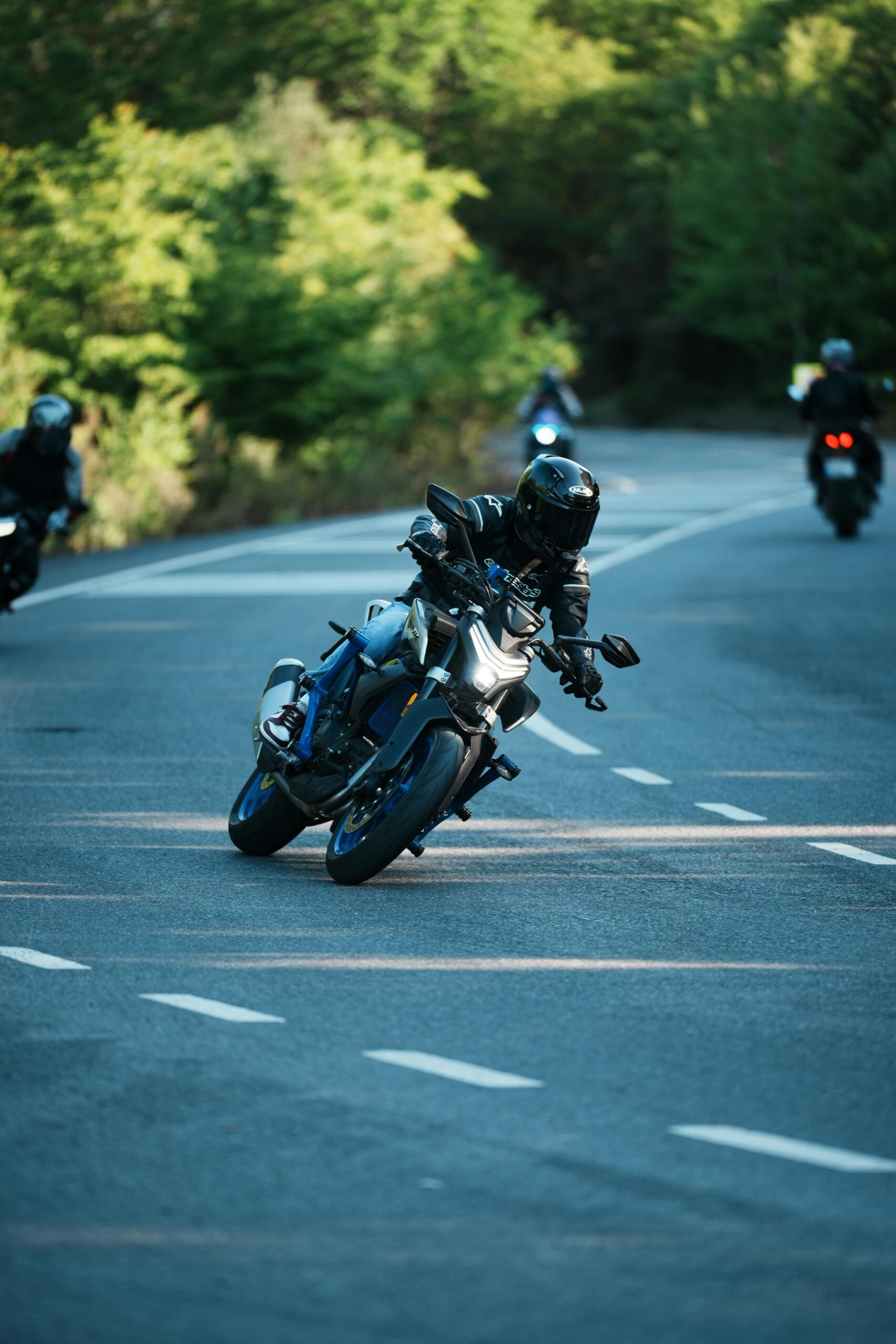 Motorcyclists racing on a curvy forest road during daytime. Action-packed and thrilling.